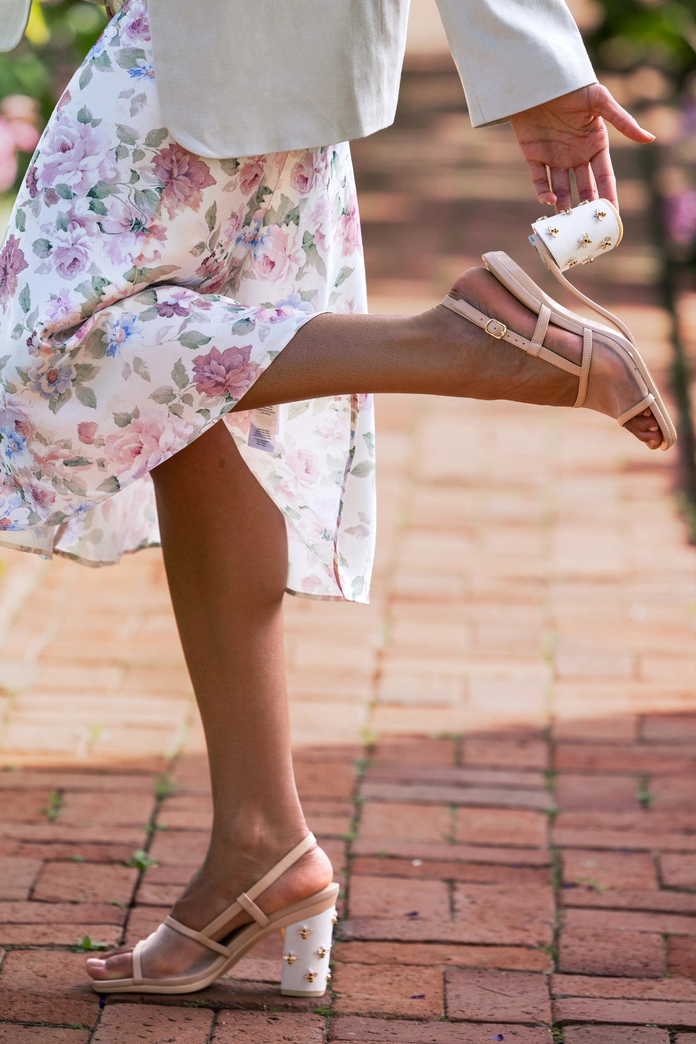Person wearing floral dress and beige mesh mule sandals on a brick path