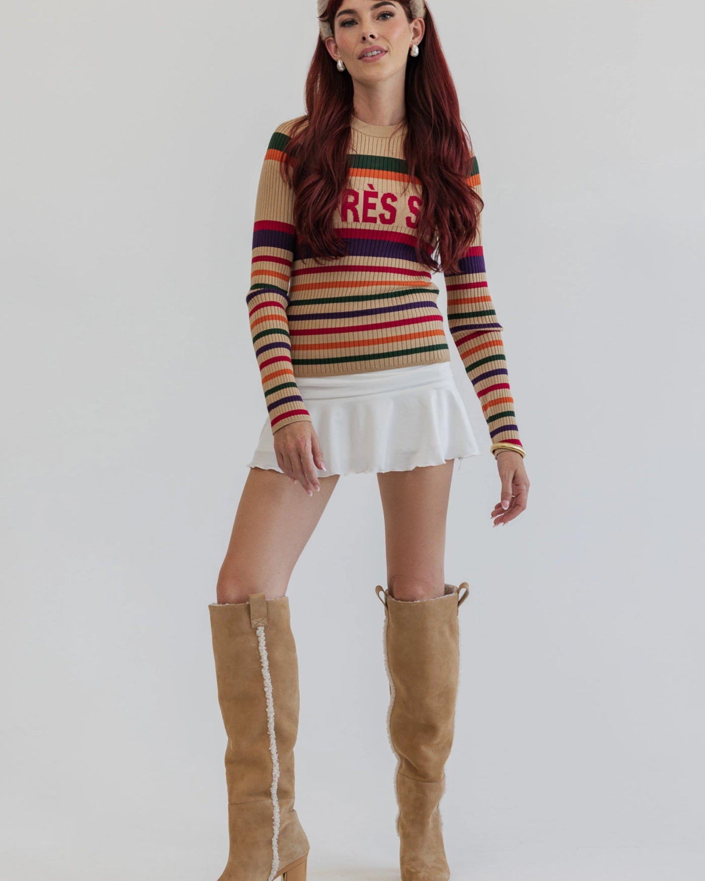 Woman wearing a striped sweater, white skirt, and tan sherpa lined knee-high boots