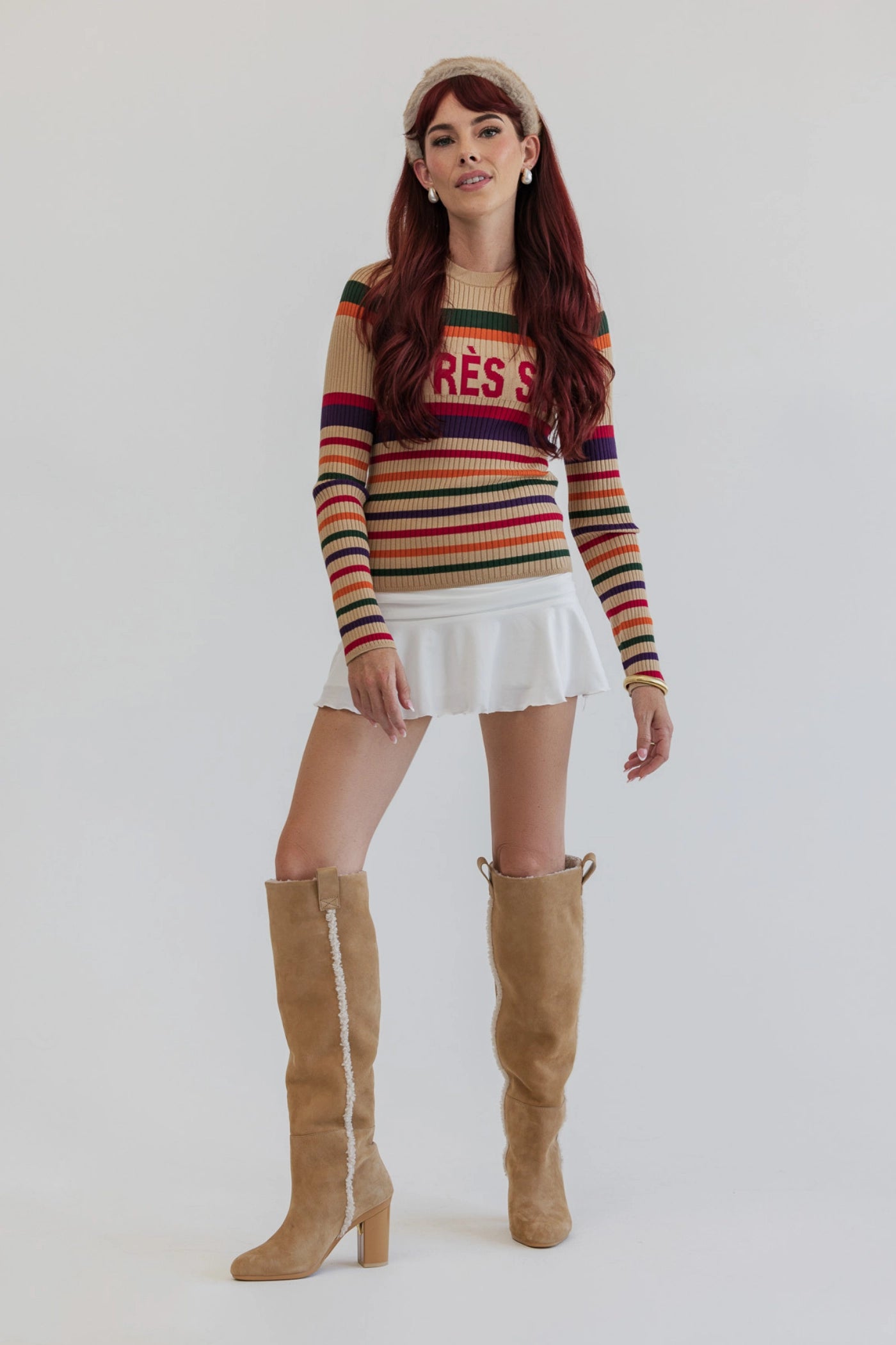 Woman wearing a striped sweater, white skirt, and tan sherpa lined knee-high boots