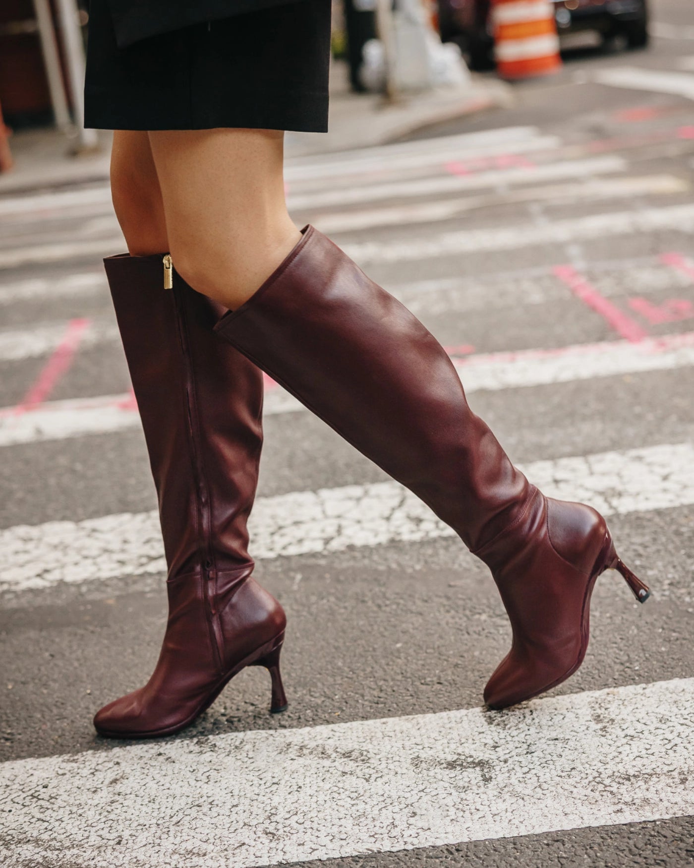Person wearing burgundy knee-high leather boots on a city street.