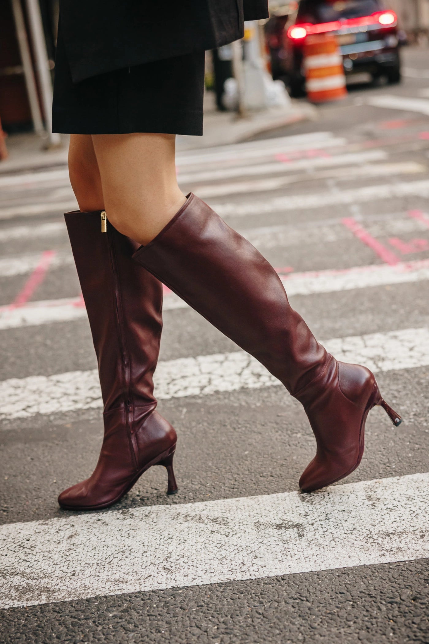Person wearing burgundy knee-high leather boots on a city street.