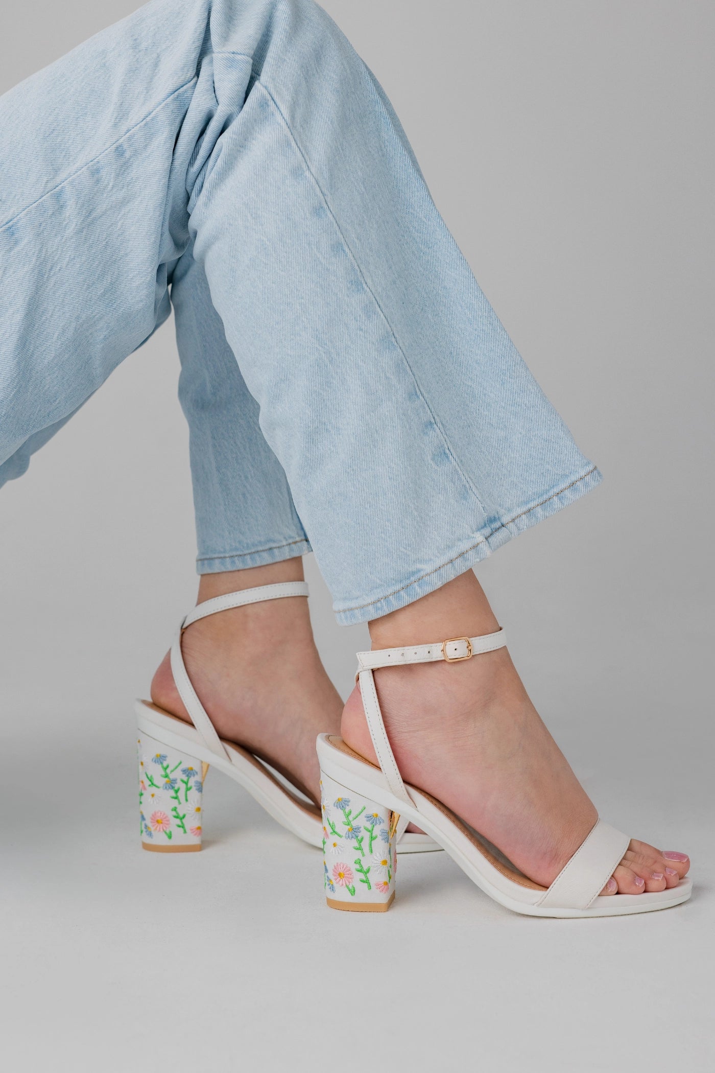 White block-heel sandals with floral patterns worn with light blue jeans on a neutral background