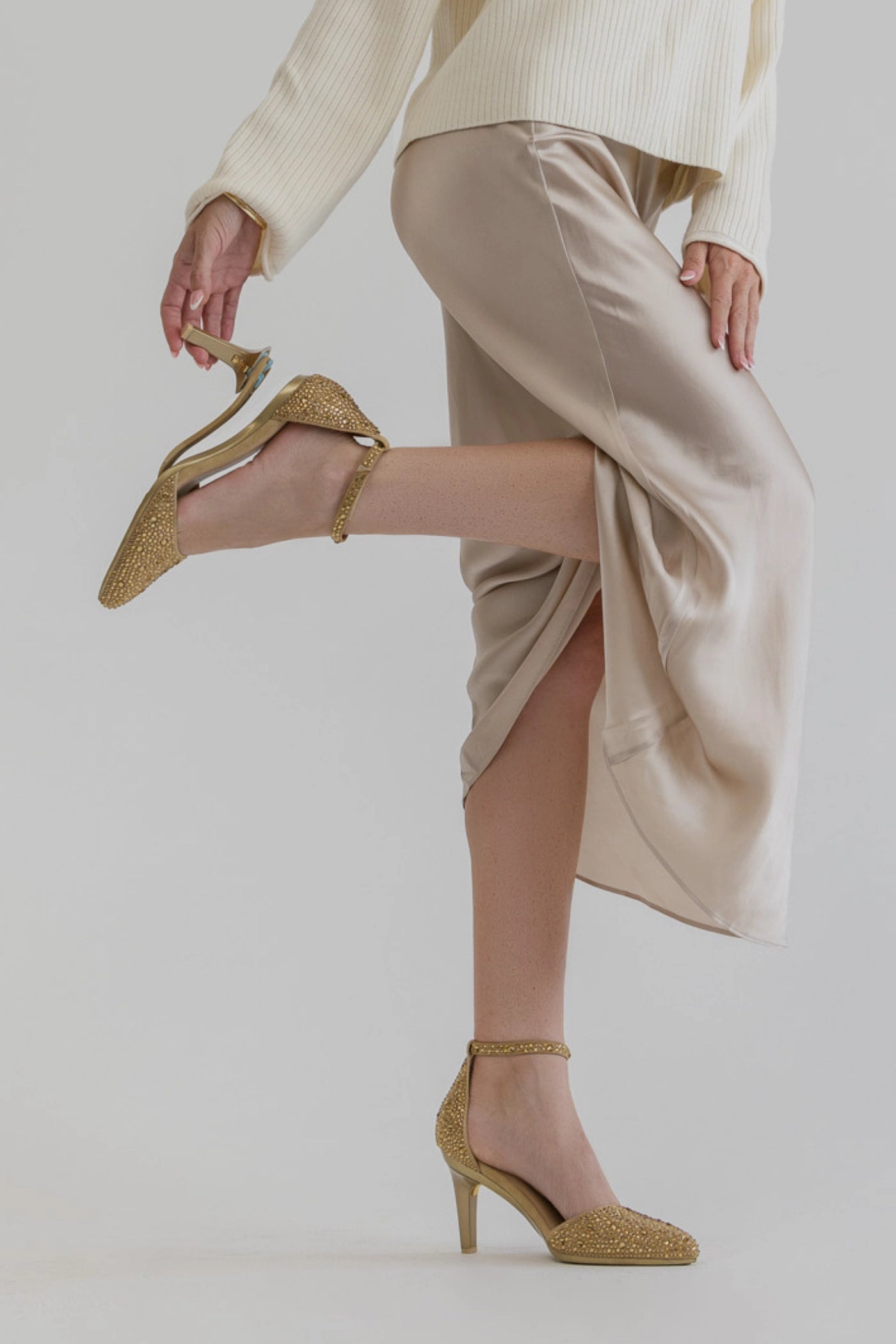 Person wearing beige high-waisted pants and gold rhinestone covered closed toe high heels