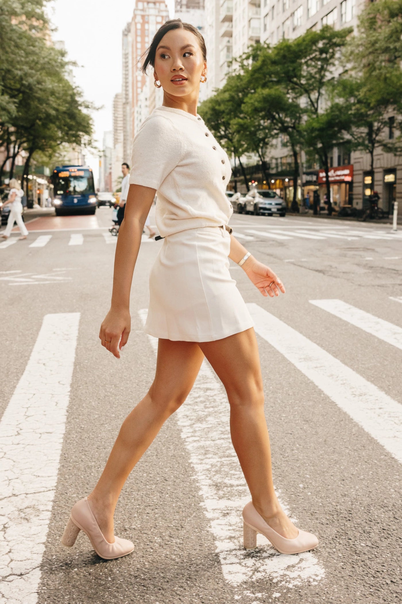 Woman in a white outfit walking on a city street with beige almond toe leather pumps