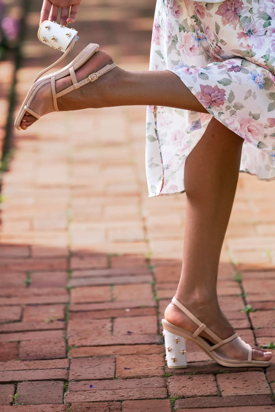 Person wearing beige sandals with floral dress on a brick pavement convertible from high heel to flat