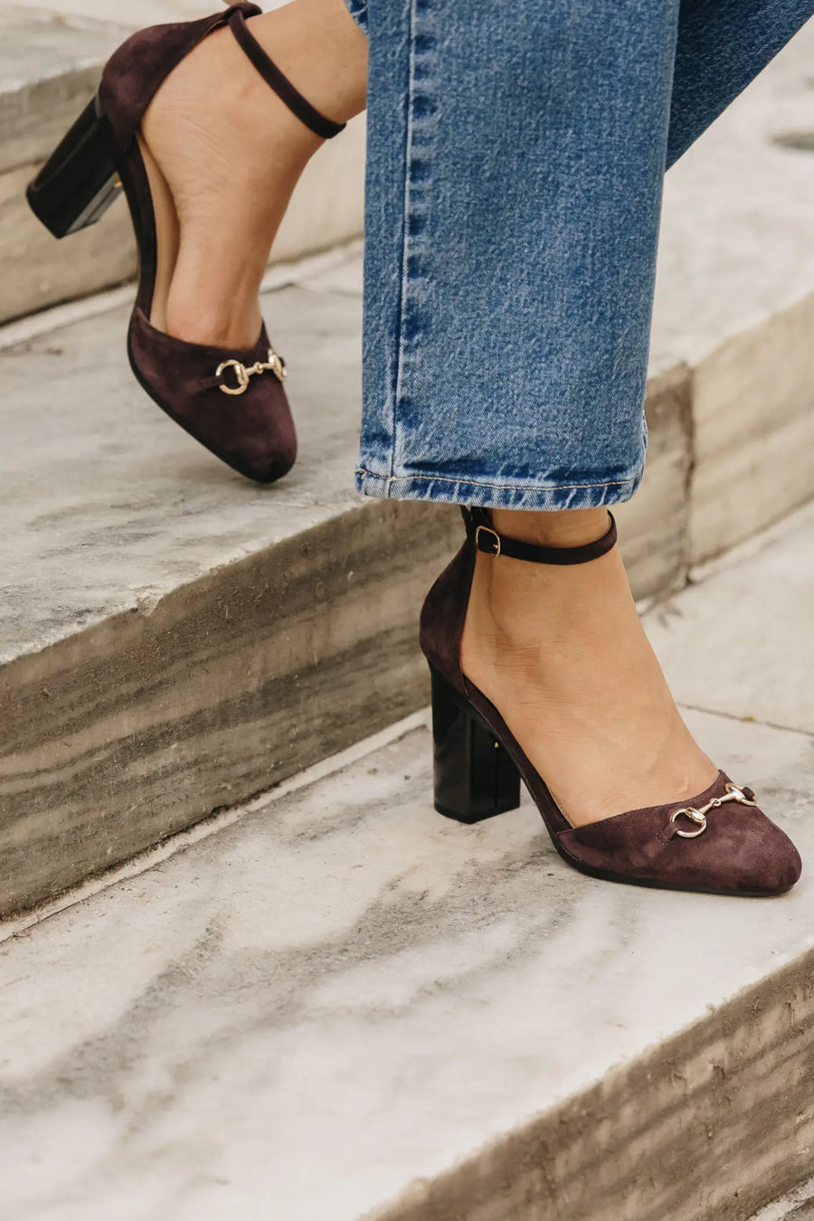 Brown suede shoes with gold buckles worn by a person on stone steps.