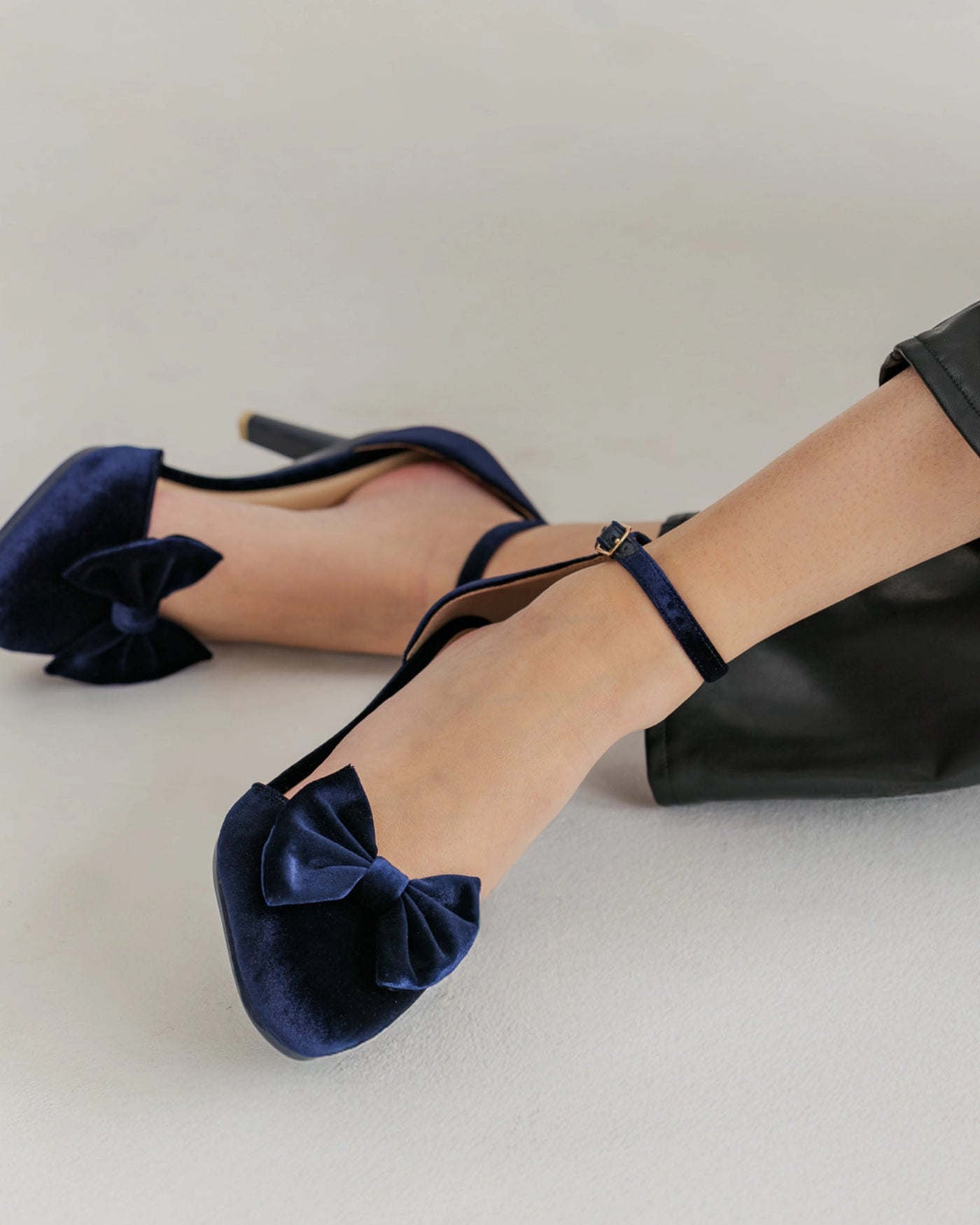 Navy blue high heels with velvet bows on the front of shoe worn by a person on a light gray background