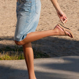 Person wearing denim shorts and tan convertible sandals on a sandy beach.